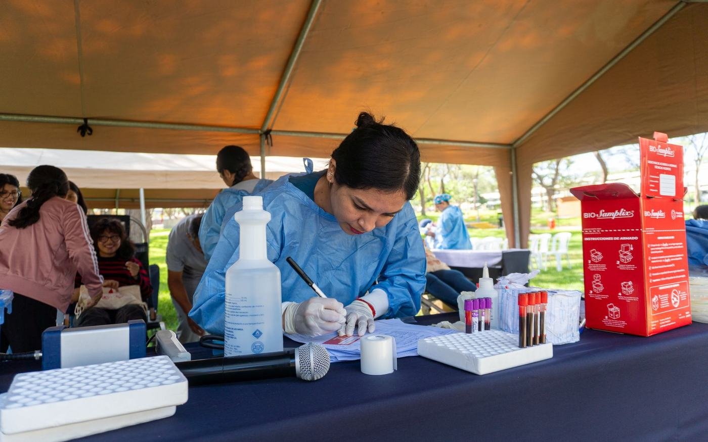 Personal de salud atiende bajo una carpa en una jornada comunitaria, con mesa de registro y material médico.