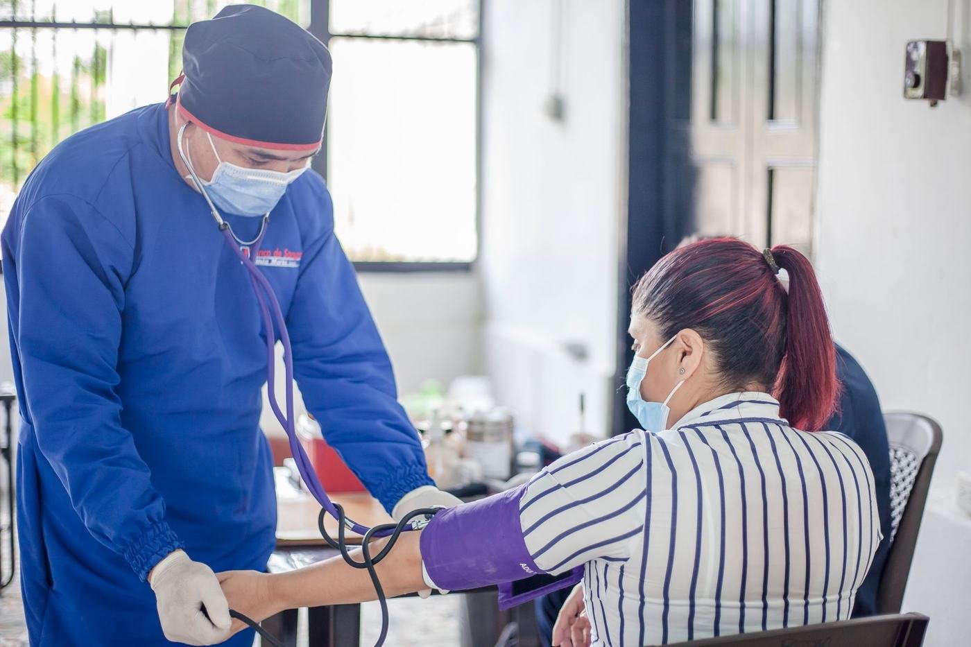Una enfermera toma la presión arterial a una joven sentada en una jornada de salud.
