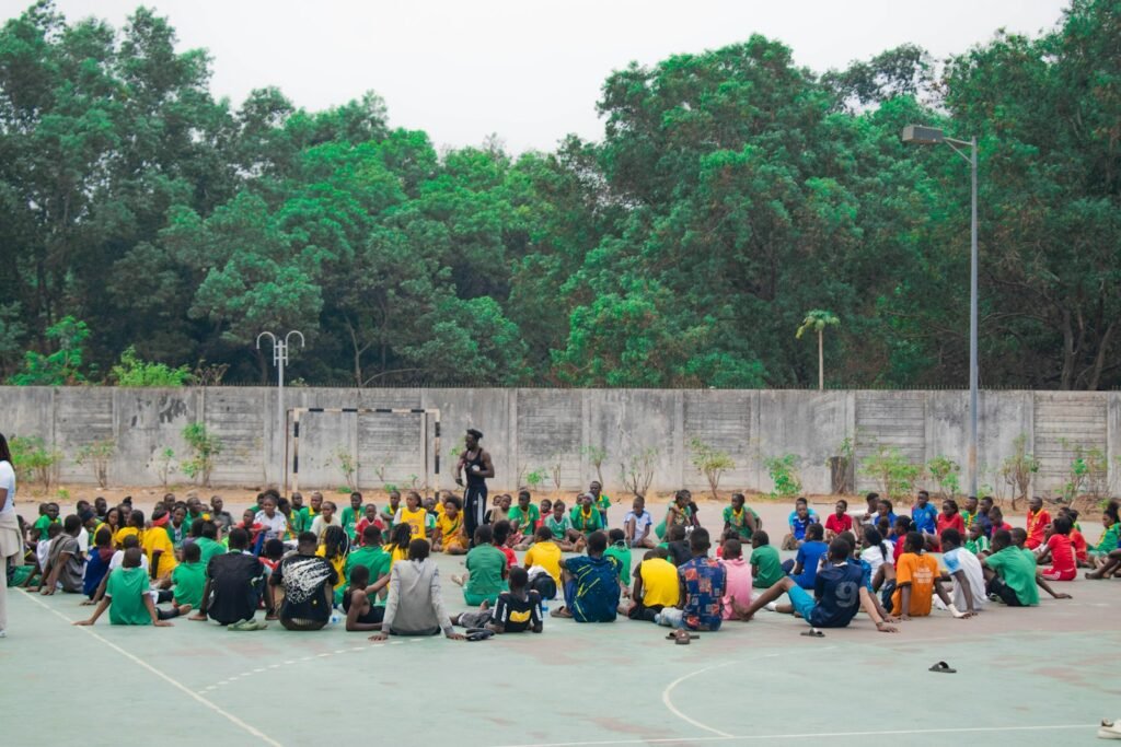Niñas, niños y jóvenes sentados en círculo en la cancha de su escuela