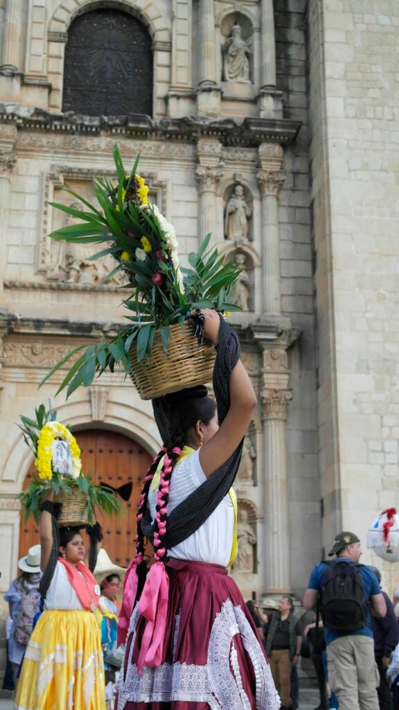 Mujer con traje tradicional y canasta de flores en la cabeza durante una calenda en Oaxaca