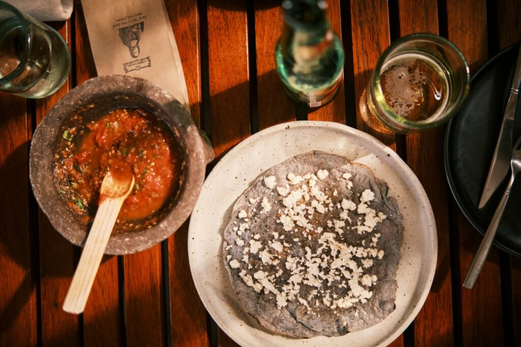 Salsa en molcajete junto a una tortilla de maíz azul con queso