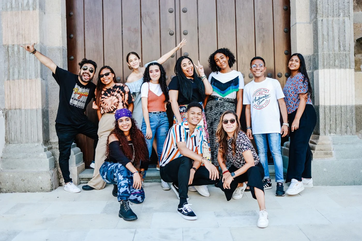 Un grupo de jóvenes mexicanos sonríe y levanta los brazos frente a un portón colonial